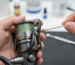 A person's hands carefully cleaning the line roller of a spinning reel with a cotton swab.