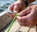 A beginner angler tying a Palomar knot with braided fishing line and a lure.